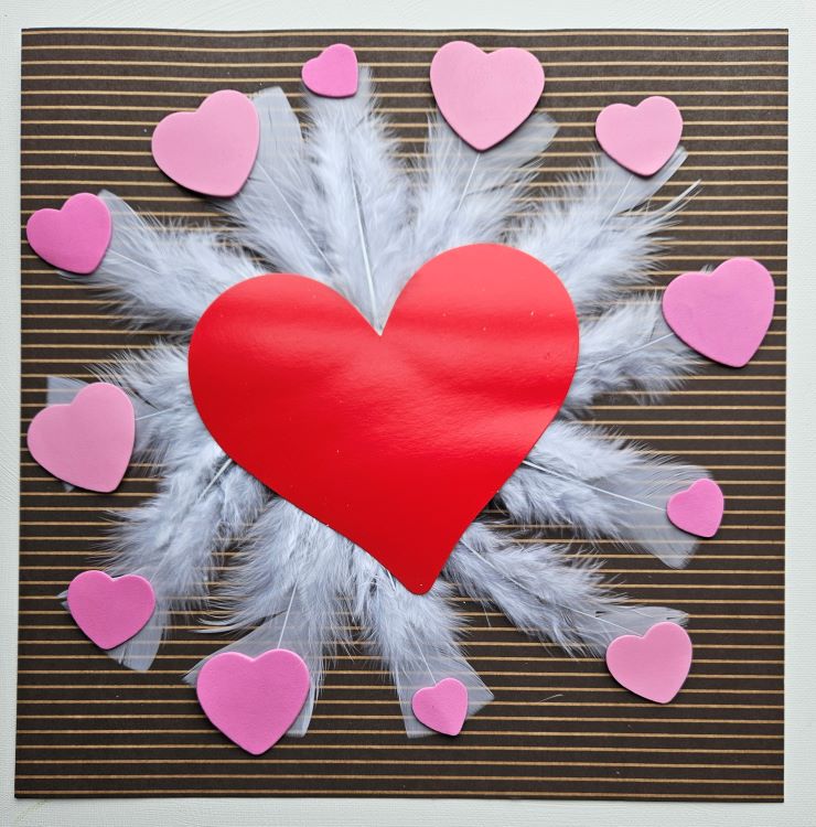 A large red heart is centered on a backdrop of white feathers, surrounded by smaller pink hearts. These elements rest on a striped brown surface.