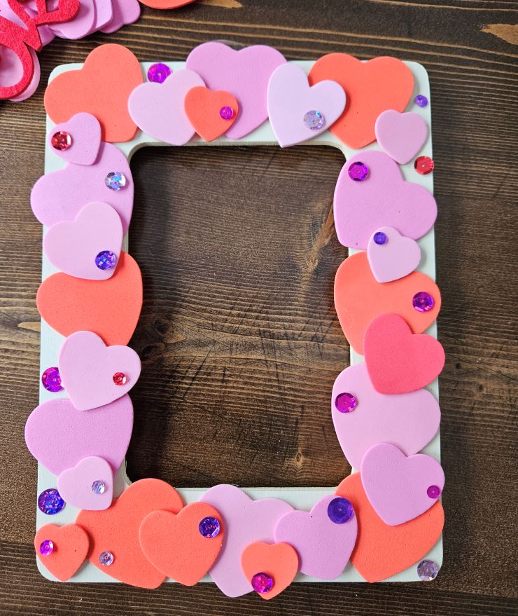 White picture frame with foam craft hearts and fake craft gemstones glued to the frame