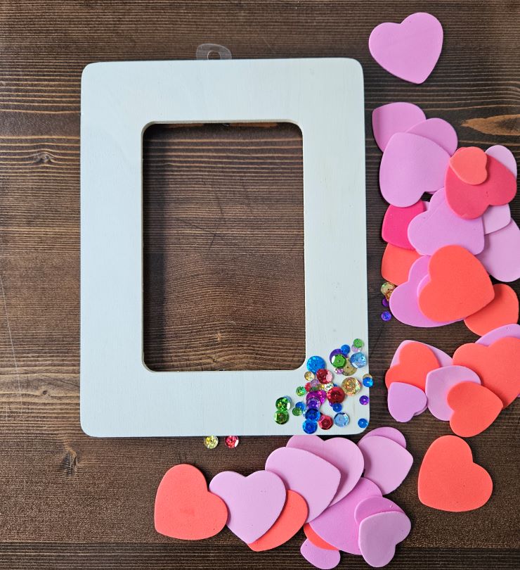 white picture frame and lots of hearts to the right of the frame on a wooden background