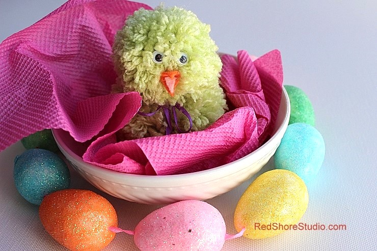 pom pom chick in a bowl with colorful plastic eggs around the bowl